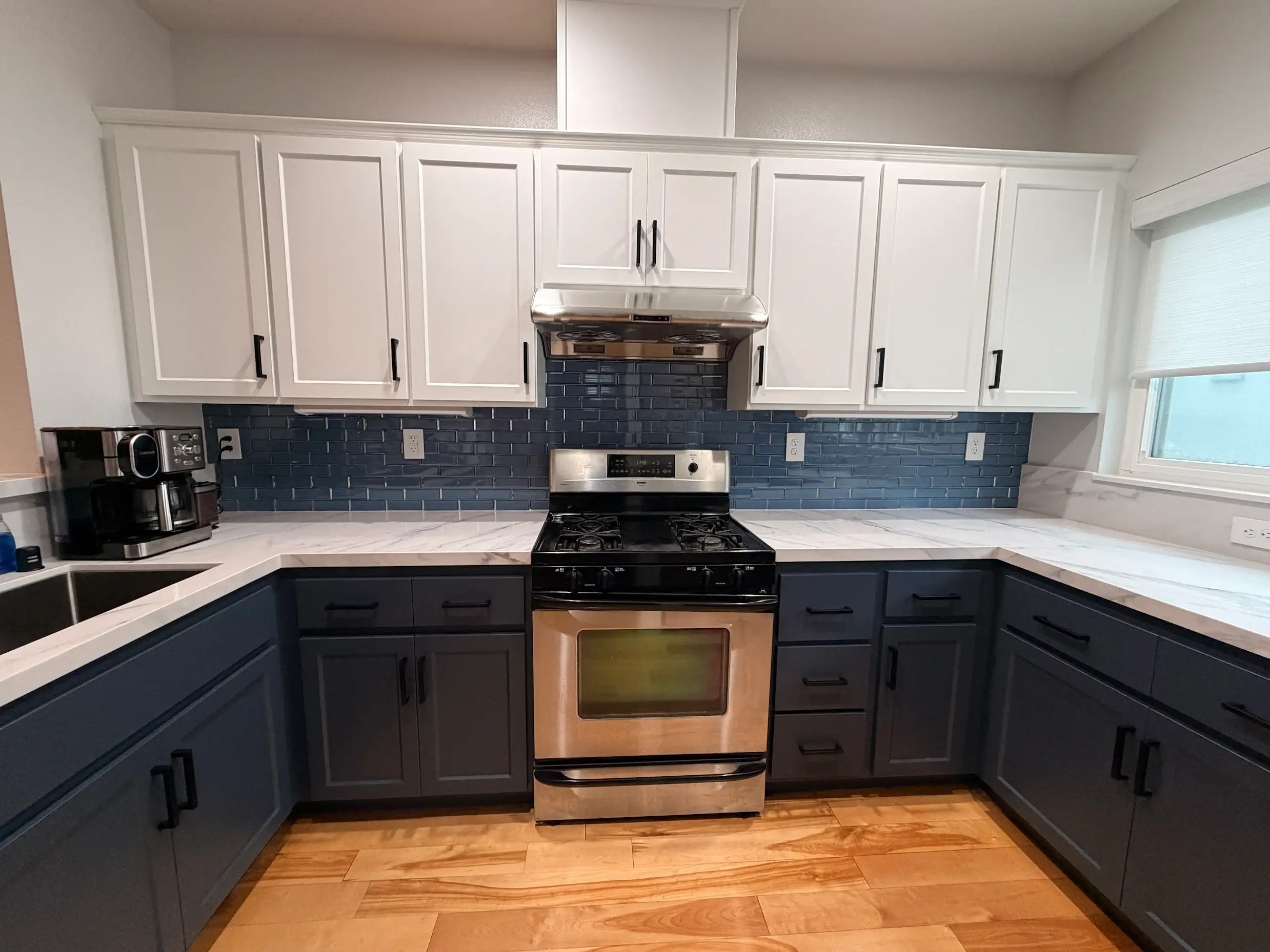 Blue and white kitchen remodel after — white upper cabinets, blue lower cabinets, and modern backsplash by Adval Construction